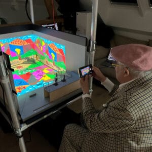 David Hockney viewing the model box contai ning "August 2021, Landscape with Shadows" Twelve iPad paintings comprising a single work © David Hockney . Photo credit: Mark Grimmer