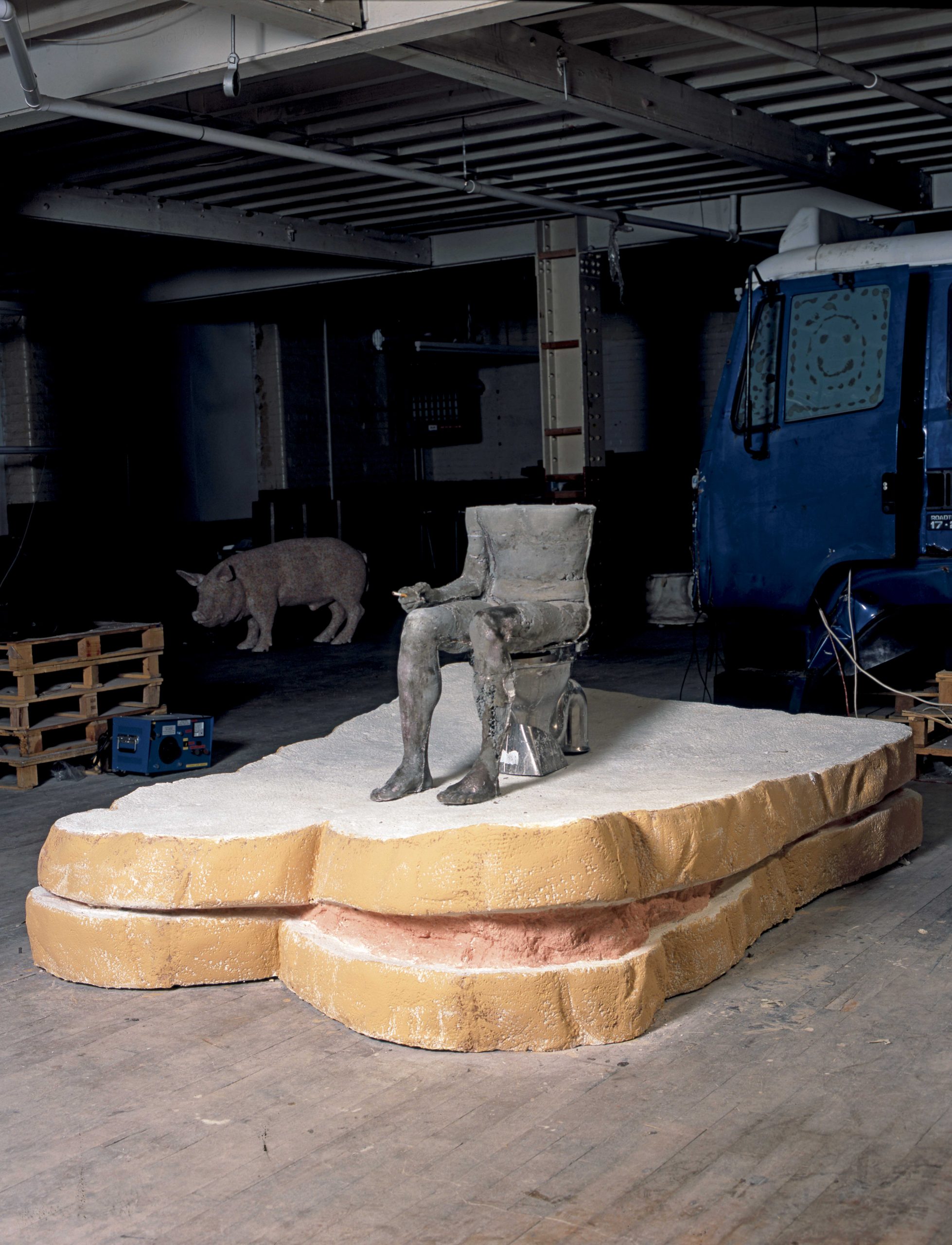 SarahLucas,Cnut,2004 Jesmonite sandwich, concrete figure, cigarette, paint, stainless steel toilet, plastic seat. Sandwich: 60 x 244 x 190 cm figure: 87 x 102 x 43 cm © Sarah Lucas, courtesy Sadie Coles HQ, London