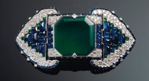 An Art Deco emerald, sapphire and diamond belt buckle-brooch, Cartier. Octagonal step-cut emerald of 38.71 carats, buff-top calibré-cut sapphires and emeralds, old and single-cut diamonds, platinum and 18k white gold (French marks), 3½ in, 1922. Unsigned, partial maker’s mark (Atelier Renault), no. 0346, red Cartier case