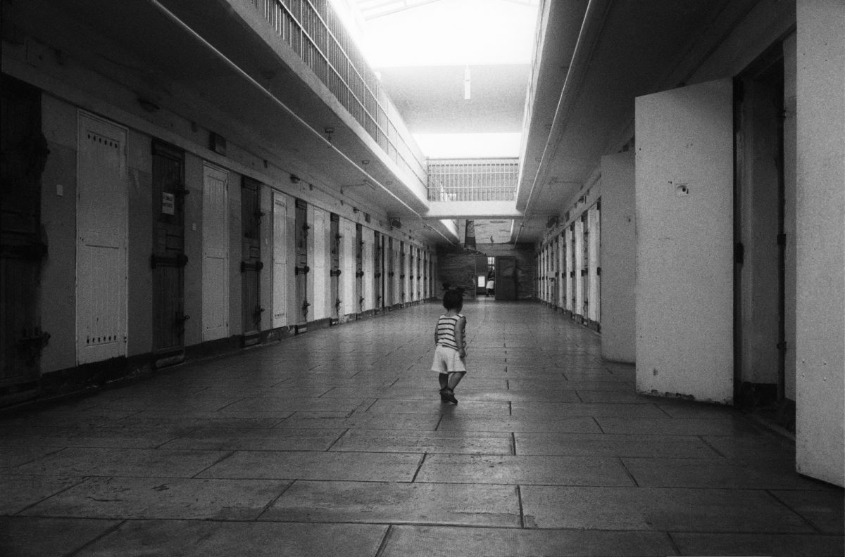Black and white photograph of a toddlerwalking along a prison corridor.