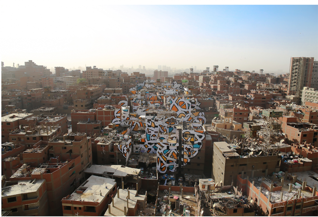 The Tunisian/French artist eL Seed’s installation Perception, was painted across 50 buildings in Cairo without the consent of the Government who have stopped street artists making work, and censure artists across many media. The installation was in an area called Manshiyat Nasr, where Coptic Christians live. They are called Zabaleen (the garbage people) but do not use this term themselves. They collect the city’s rubbish and recycle it, yet are discriminated against because of their work, and they are seen as dirty. The text eL Seed used is from Saint Athanasius of Alexandria, a 3 rd century Coptic Bishop and states: (Anyone who wants to see the sunlight clearly needs to wipe his eye first). The anamorphic image took the artist and a team of workers over three weeks in install, and it could clearly be seen from the nearby Moqattam Mountain. Perception 2016 Installation, paint on 50 buildings